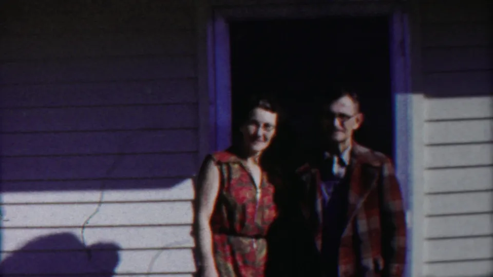 The final frame holds on the couple in the doorway, their clothing and faces softened by grain and shadow.
