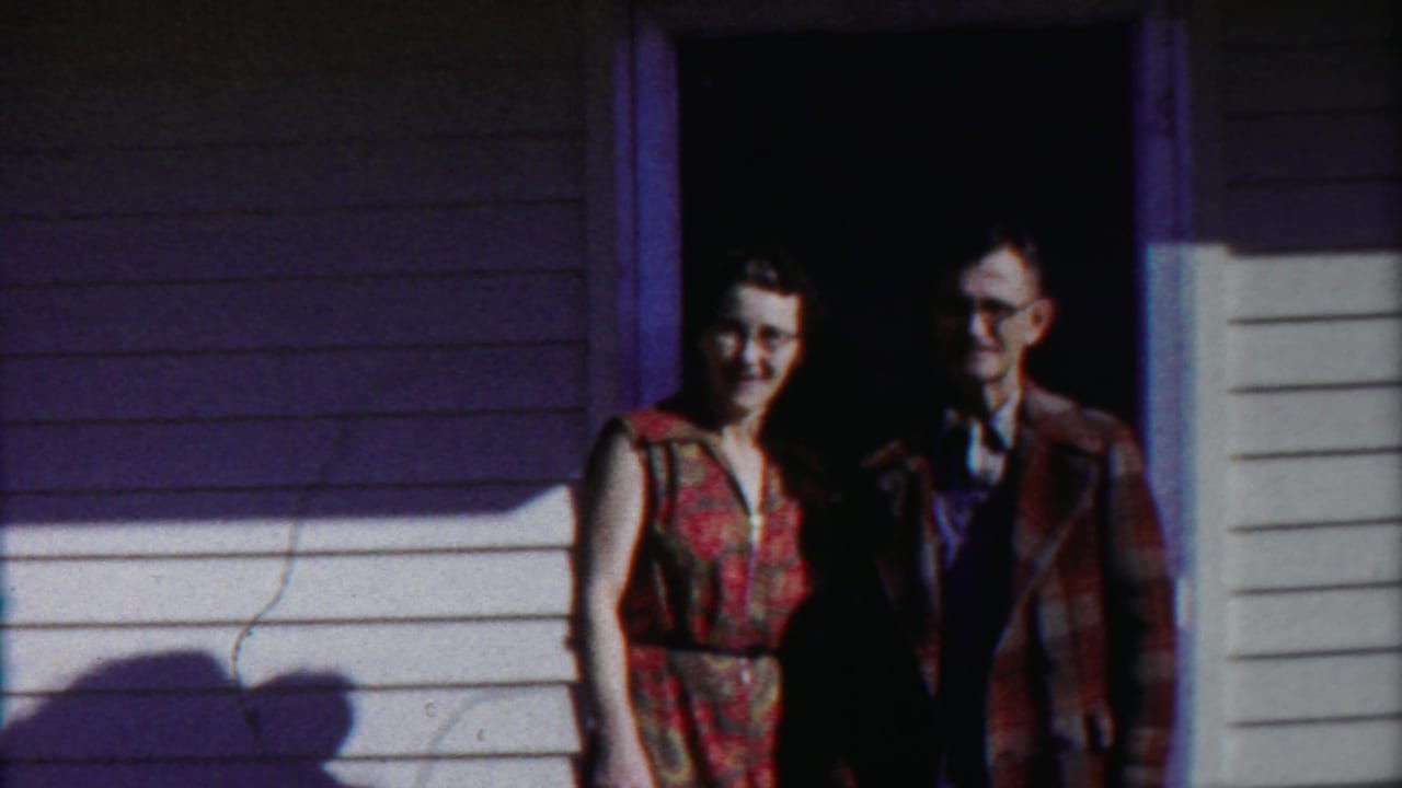 In 1958 Cheyenne County, Kansas footage, a woman in a floral dress and a man in a plaid coat stand in a doorway.