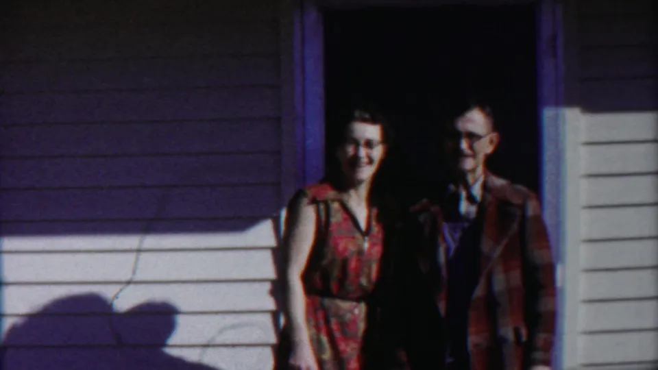 The woman and man smile toward the camera from a doorway in 1958 Cheyenne County, Kansas home-movie footage.