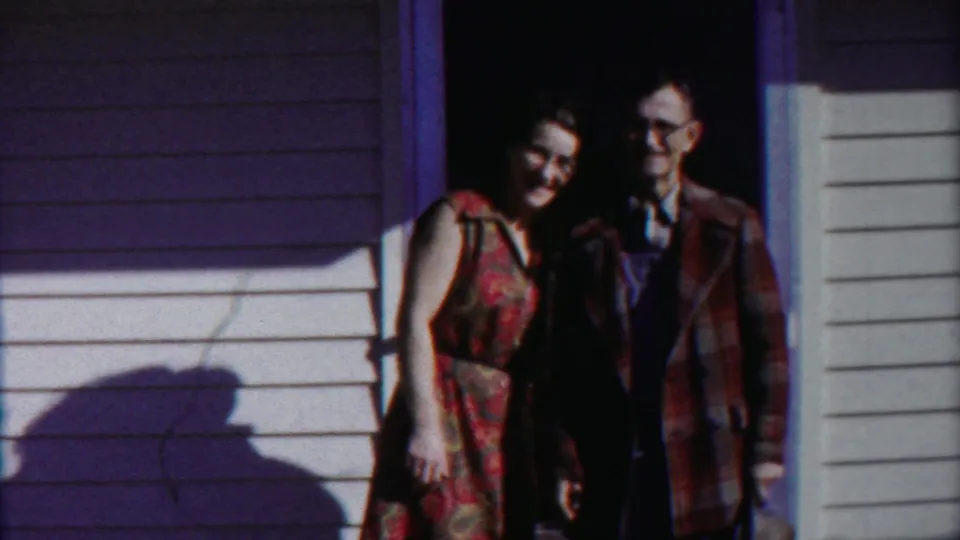 A woman in a sleeveless floral dress leans slightly toward a man in glasses in this Kansas 1958 doorway scene.