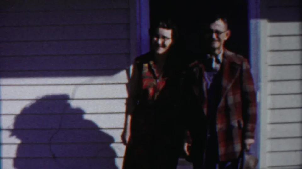 The adults remain close in the doorway, partly shadowed against white siding in Cheyenne County, Kansas home-movie footage.