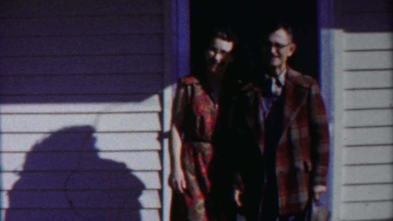 Couple standing in a dark doorway beside white siding and a large cast shadow.