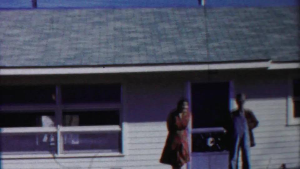 A wider 1958 Kansas frame shows the adult couple near the porch, window, white siding, and sloped roofline.