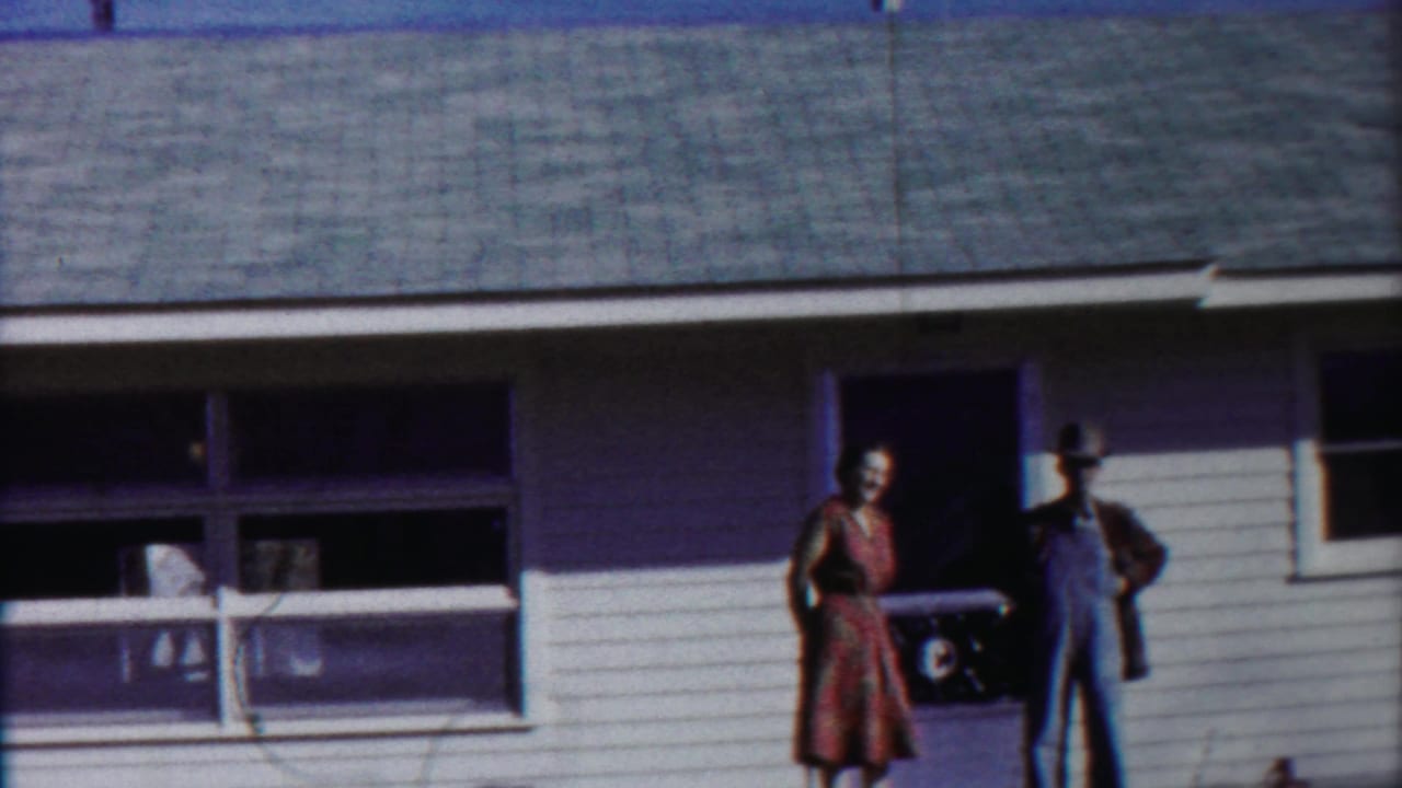 In 1958 Cheyenne County, Kansas footage, a woman in a dress and a man in overalls stand outside a modest white-sided house.