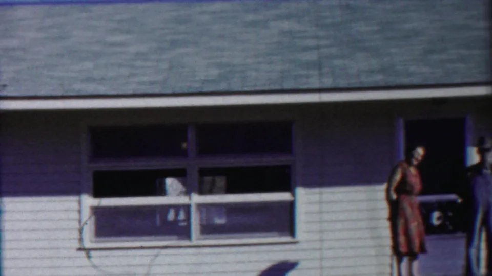 The Kansas home-movie frame shows the house exterior with broad windows and partially cropped adults at the doorway area.