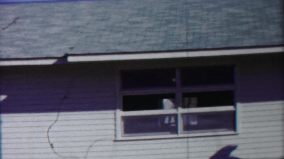 The 1958 Cheyenne County frame centers on the white-sided house front, showing windows, roof shingles, and strong daylight shadow.