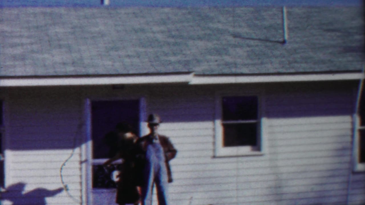 A woman gestures near the doorway while a man in overalls stands beside the entrance.