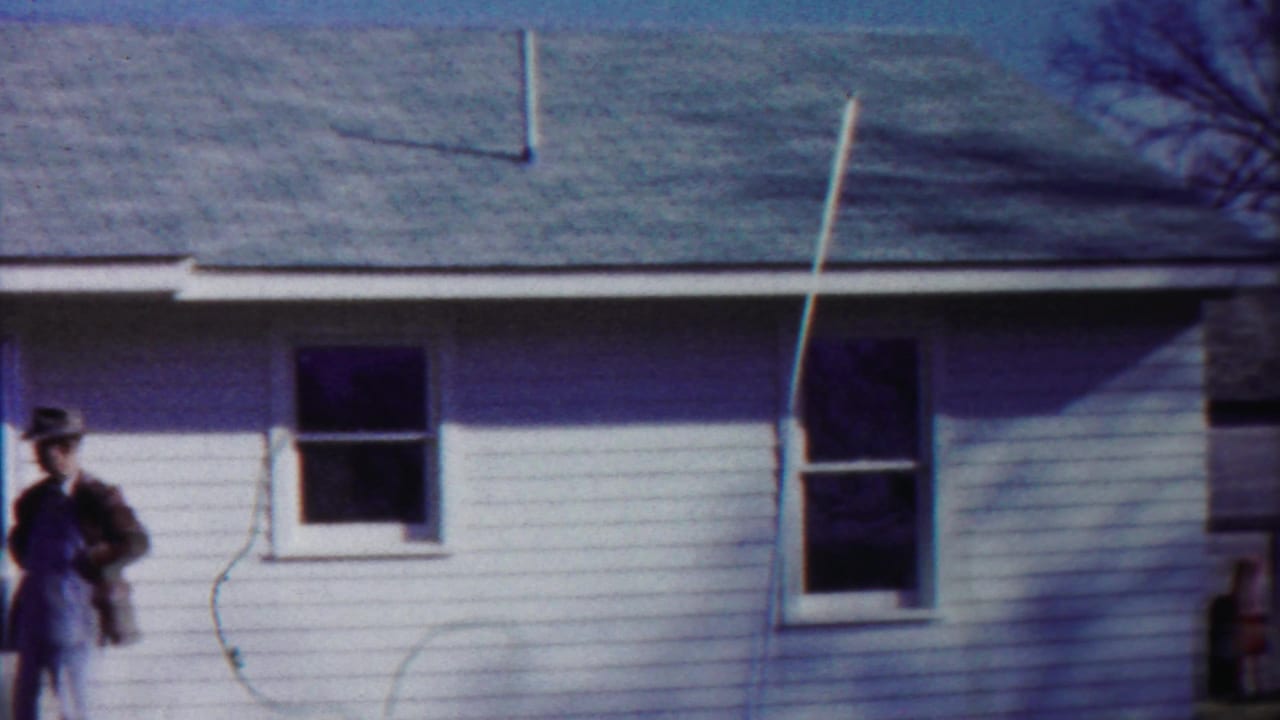 1958 Cheyenne County, Kansas street view with a white clapboard building, overhead decorations, a man at frame edge, and distant WAREHOUSE sign.