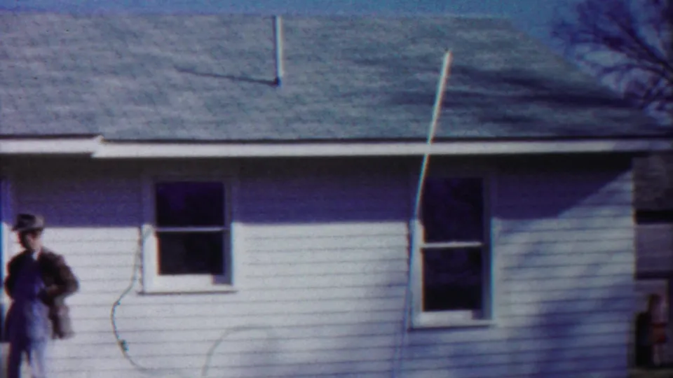 1958 Cheyenne County, Kansas street view with a white clapboard building, overhead decorations, a man at frame edge, and distant WAREHOUSE sign.