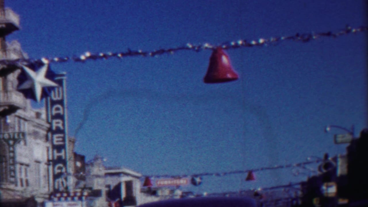 Decorated downtown street with a vertical WAREHOUSE sign, hanging bells, storefronts, and cars below.