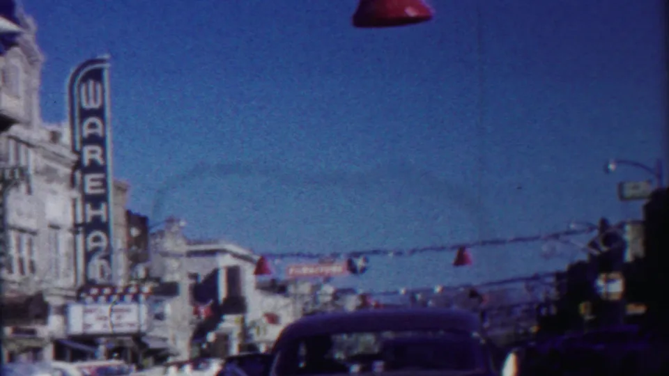 1958 Cheyenne County street scene showing the WAREHOUSE sign, overhead decorations, storefronts, and a dark mid-century automobile.
