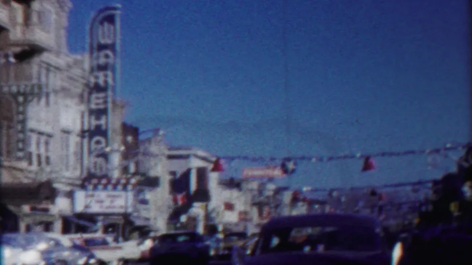 1958 Kansas downtown view with the WAREHOUSE sign, red hanging bells, strings of lights, storefronts, and vintage cars along the street.