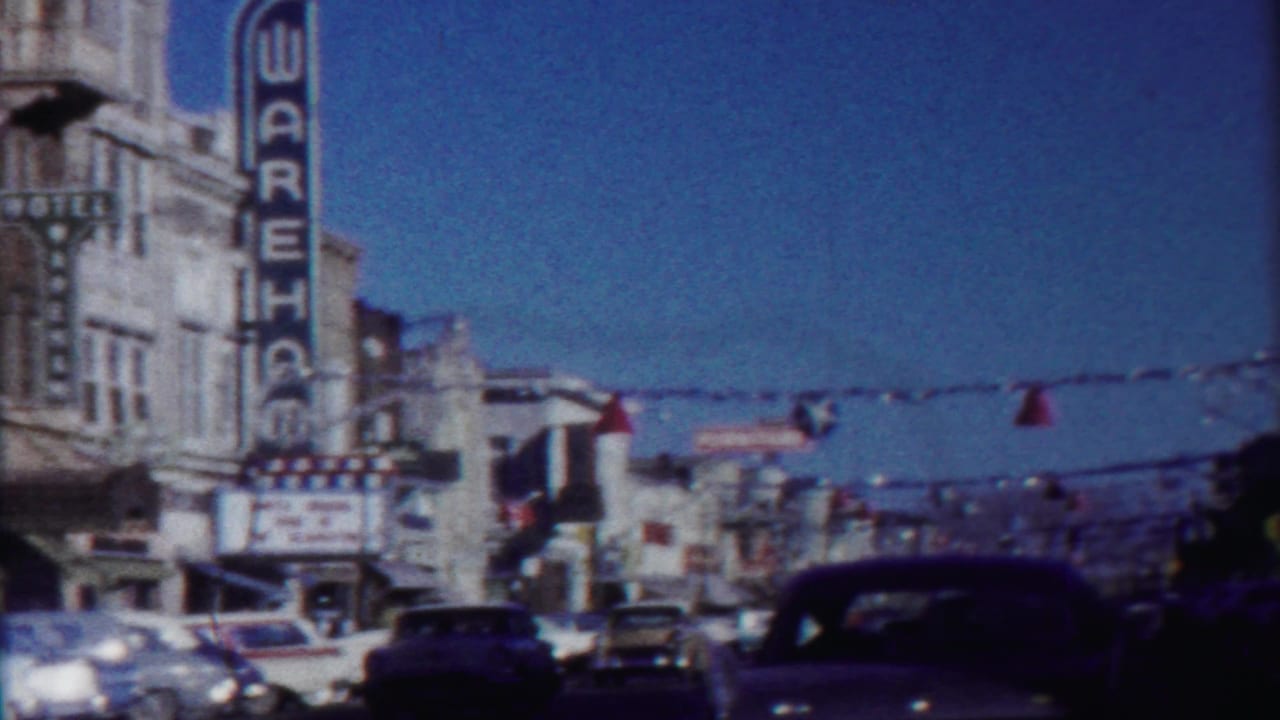 1958 Cheyenne County, Kansas street view with a WAREHOUSE theater sign, vintage cars, storefronts, and celebration decorations overhead.