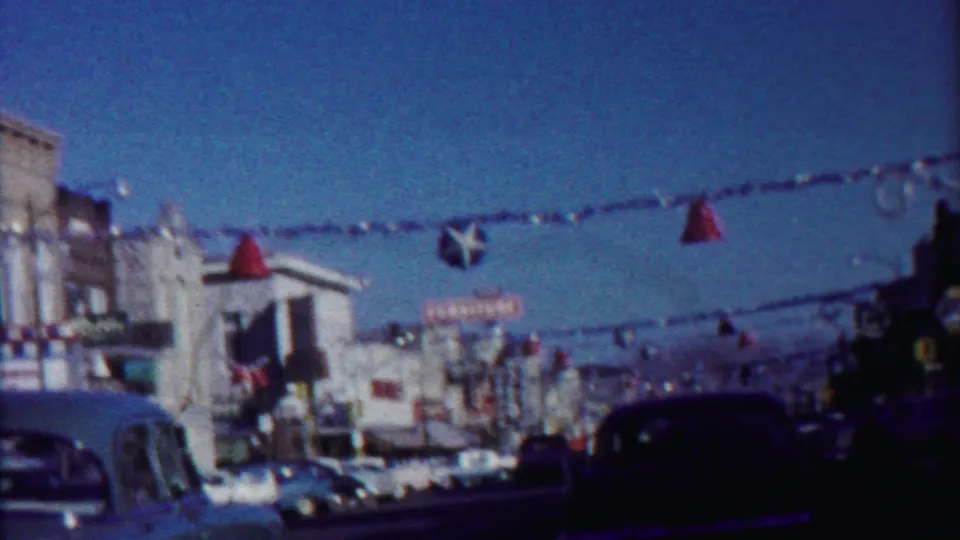 Late-1950s Kansas street view with a dark foreground car, hanging decorations, storefronts, and theater signage partly visible.
