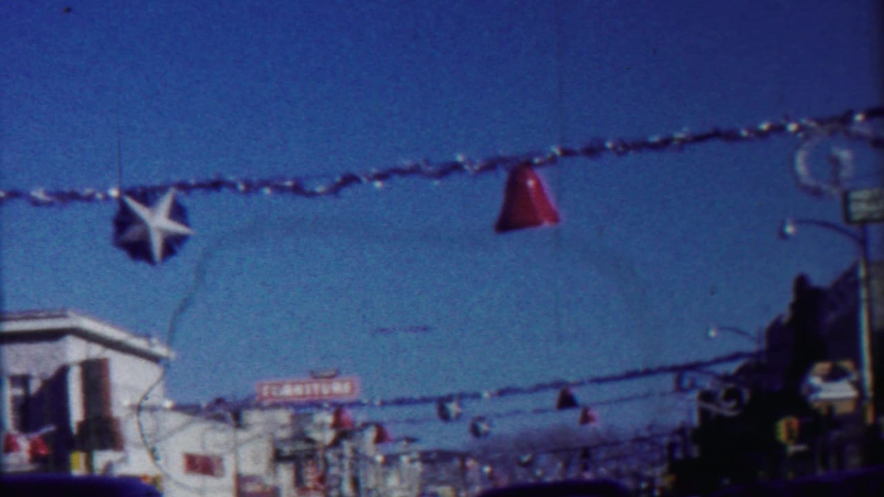1950s home-movie frame showing a decorated Cheyenne County street with overhead garland, star ornaments, storefronts, and vehicles.