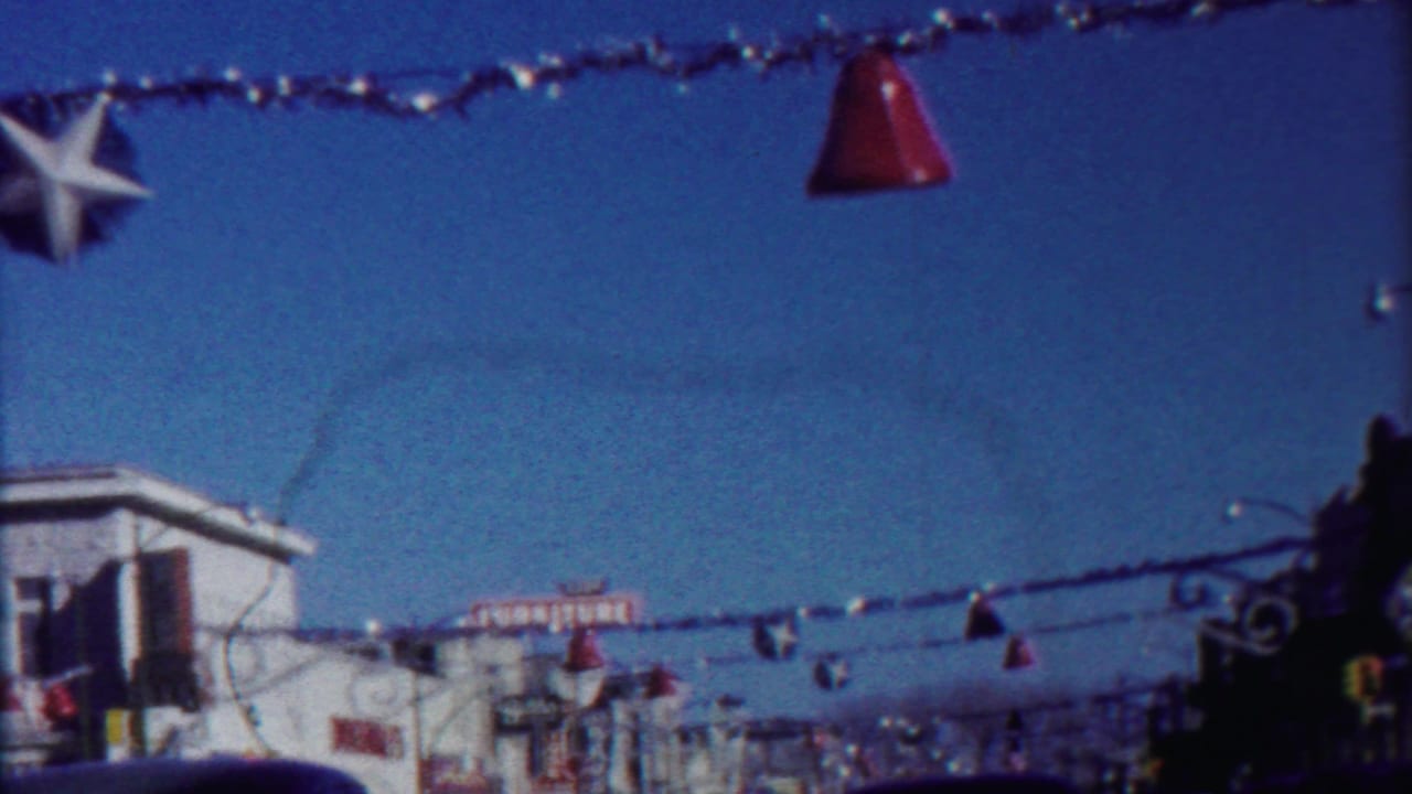 End frame of the 1958 Kansas street-driving clip, with suspended decorations, a bright sky, storefronts, and cars along the road.