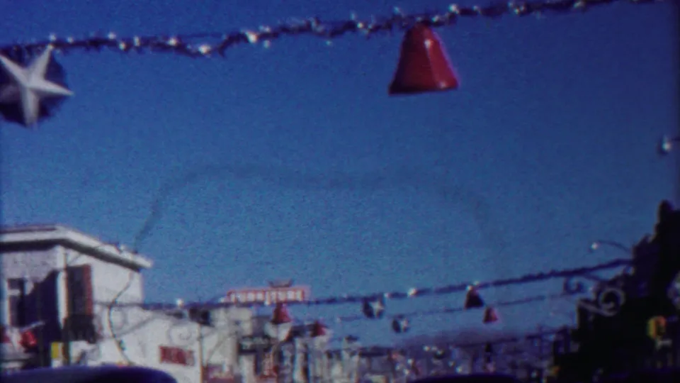 End frame of the 1958 Kansas street-driving clip, with suspended decorations, a bright sky, storefronts, and cars along the road.