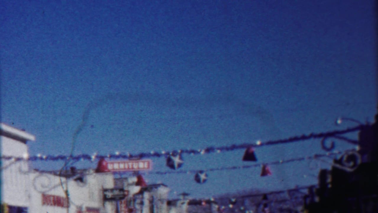 1958 Kansas home-movie frame showing suspended Christmas ornaments over a sunlit commercial street.