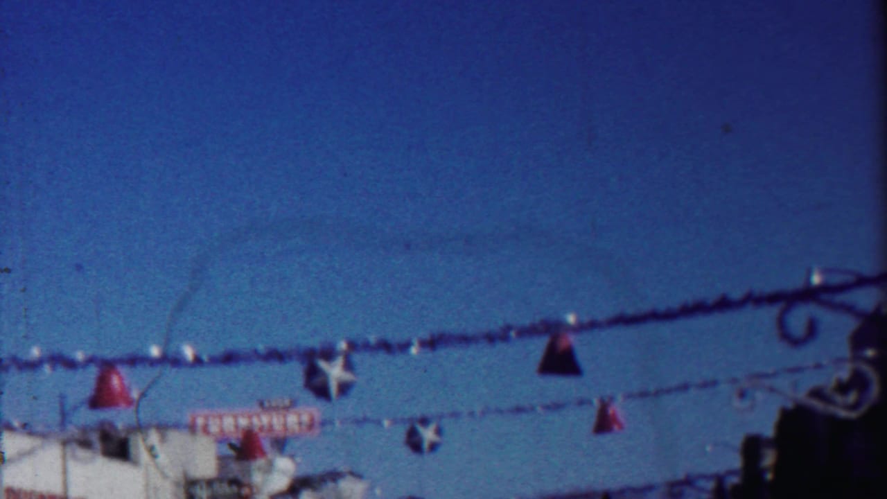 1958 Cheyenne County, Kansas 8mm frame showing festive garlands, red bell ornaments, white stars, and a partial furniture sign below.