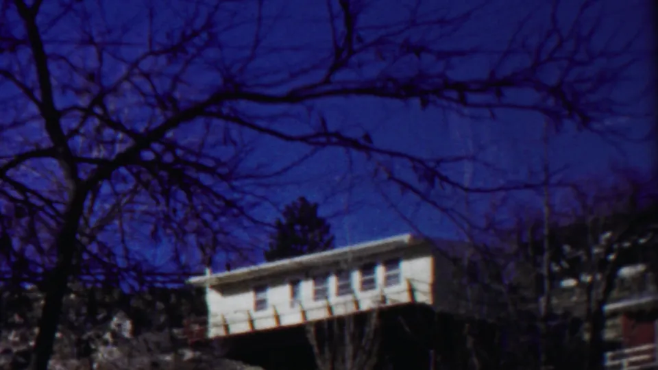 1958 Cheyenne County, Kansas frame of a white house partly obscured by bare branches, with another structure at the right edge.
