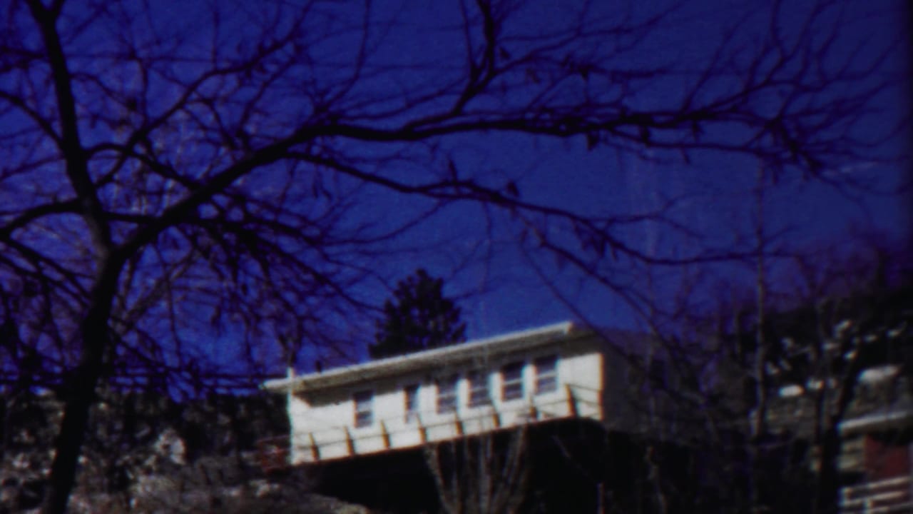 1958 Cheyenne County, Kansas 8mm frame showing a white house behind bare winter branches and a saturated blue sky.