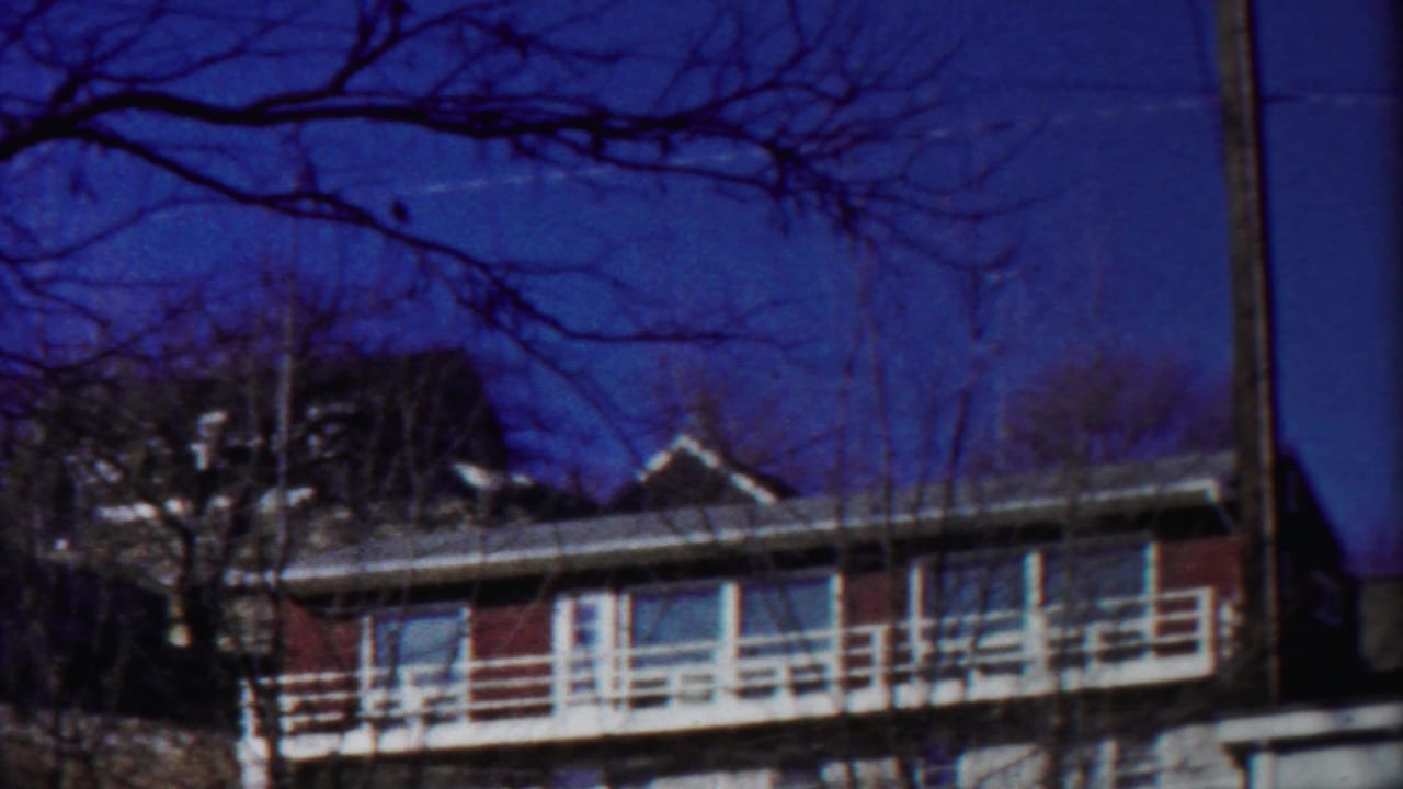 1958 Kansas 8mm frame showing a red-sided house or building with white balcony railings behind winter-bare trees.