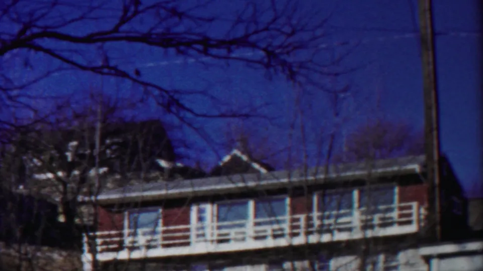 1958 Kansas 8mm frame showing a red-sided house or building with white balcony railings behind winter-bare trees.