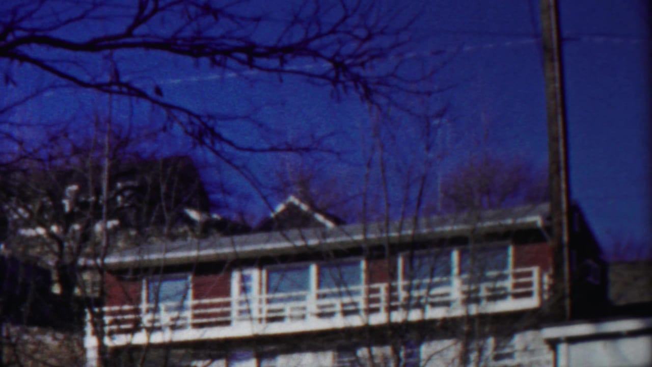 Steady 8mm frame of a Cheyenne County apartment facade with balcony railings and leafless branches in front.