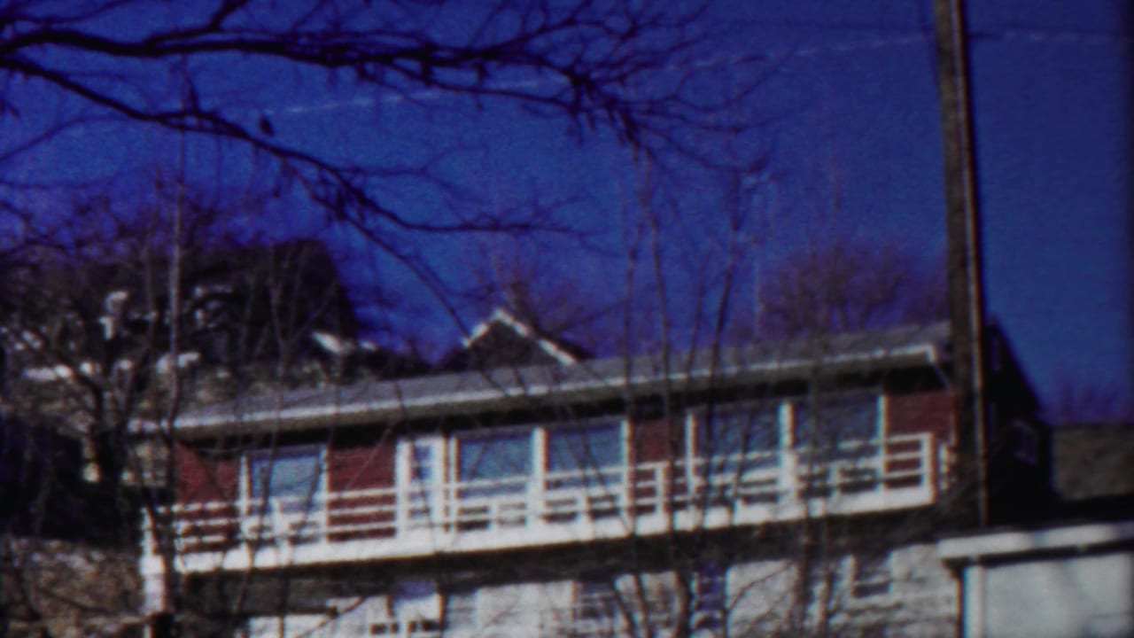 Cheyenne County 8mm frame showing the apartment exterior, roofline, balcony rails, and dark foreground branches.