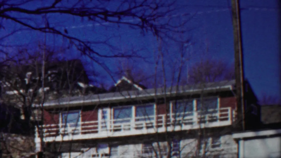 Cheyenne County 8mm frame showing the apartment exterior, roofline, balcony rails, and dark foreground branches.