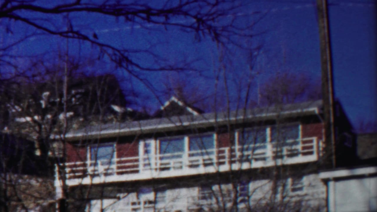Two-story residential building with white balcony, bare branches, and blue sky.