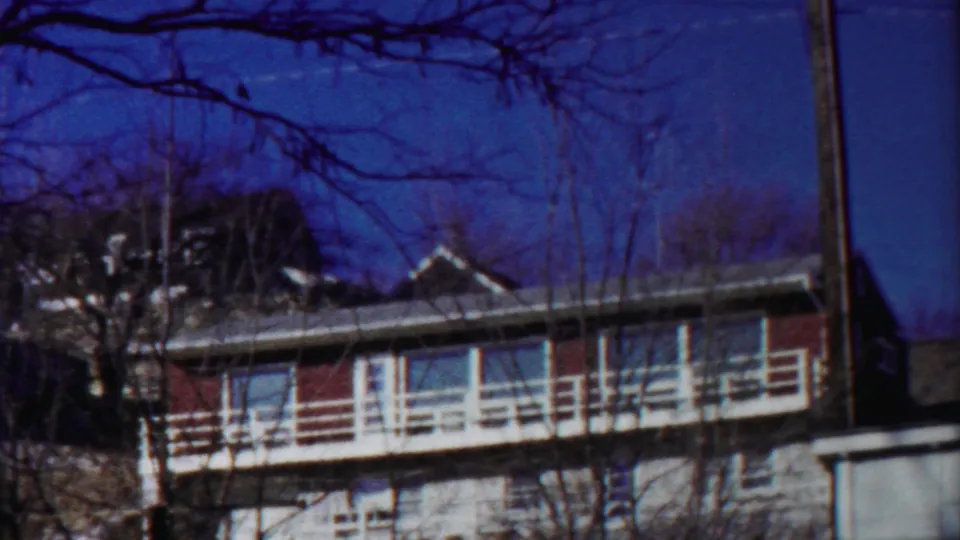 1958 Cheyenne County, Kansas home-movie frame showing a two-story house, white balcony railing, bare trees, and deep blue sky.