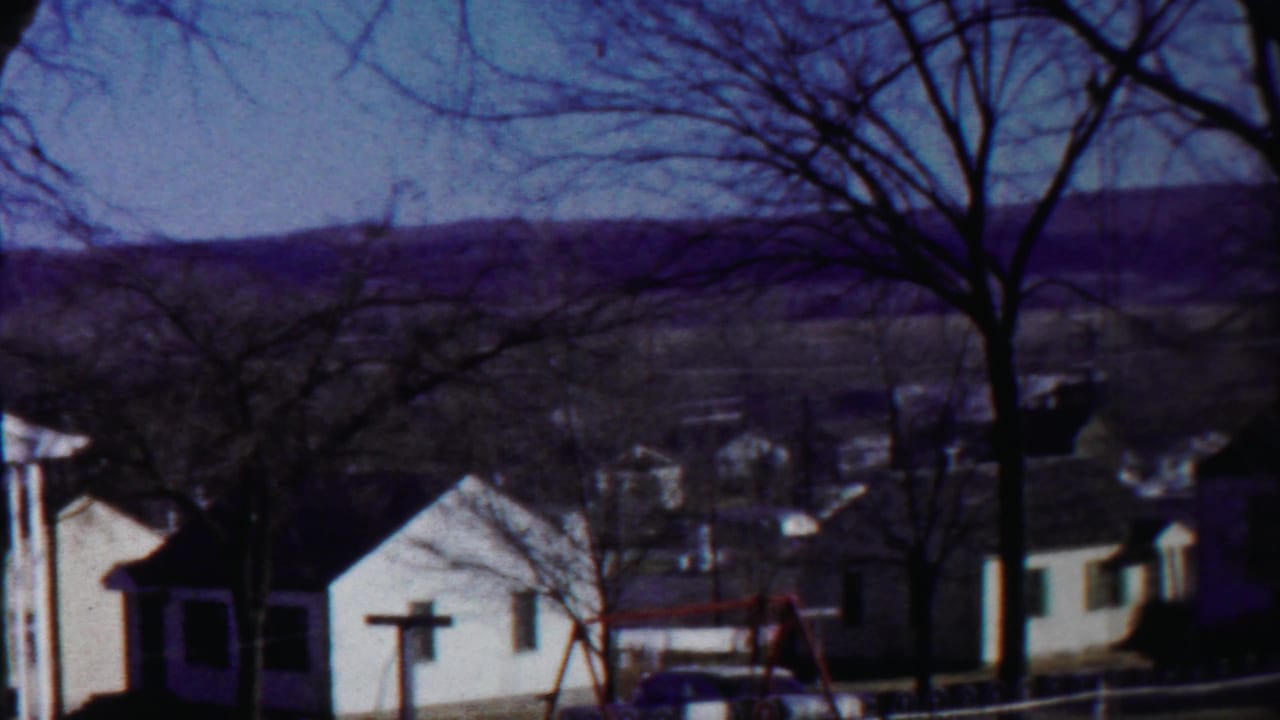 A 1958 Kansas home-movie view shows small residential buildings, winter-bare trees, distant hills, and a pale blue sky.