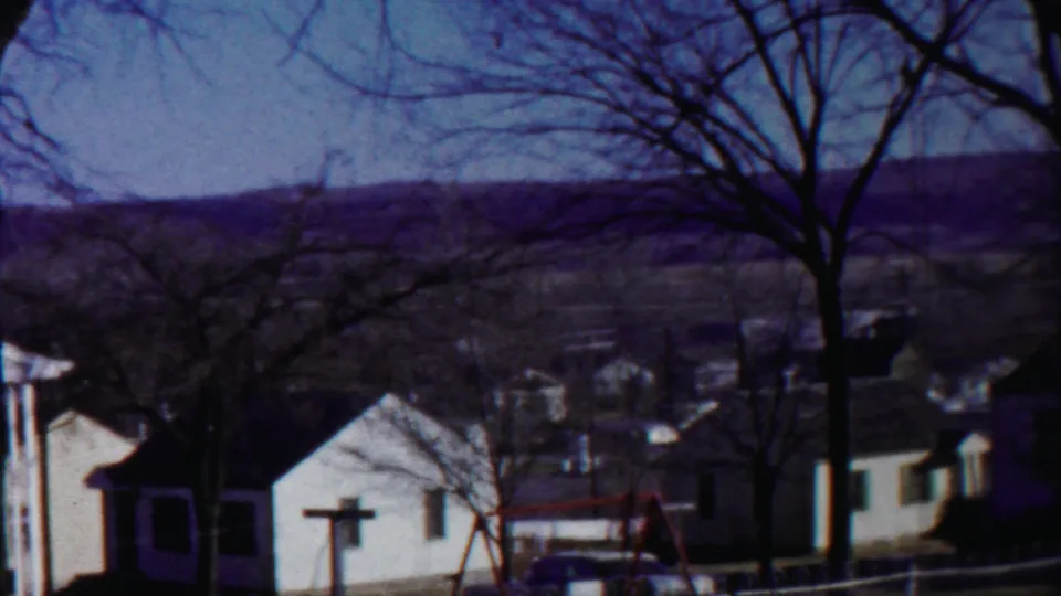 A 1958 Kansas home-movie view shows small residential buildings, winter-bare trees, distant hills, and a pale blue sky.