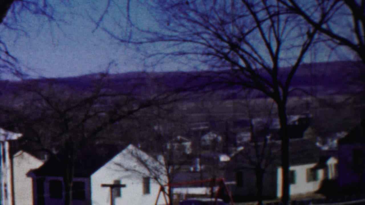 A quiet 1958 Kansas neighborhood scene shows houses, winter-bare trees, utility lines, and a low hill beyond town.