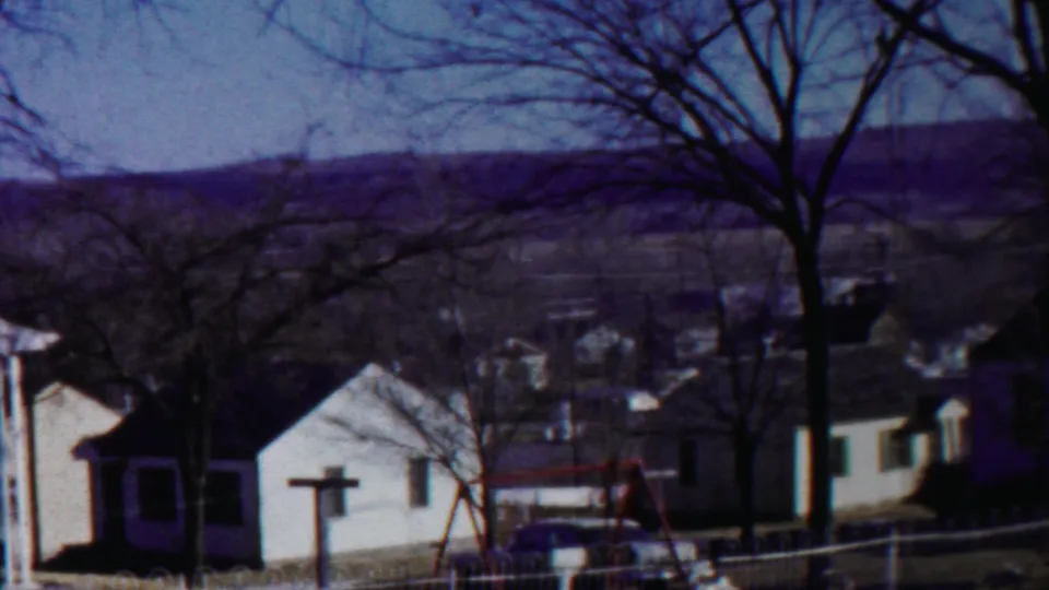 1958 Cheyenne County, Kansas home-movie view of modest houses, leafless trees, a small fence, swing set, and low hills beyond town.