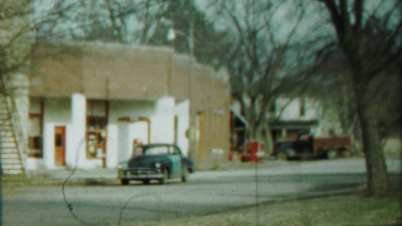 Cheyenne County, Kansas 8mm frame showing a curbside sedan, low storefront, bare trees, and a quiet roadway in 1958.