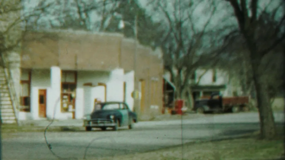 Cheyenne County, Kansas 8mm frame showing a curbside sedan, low storefront, bare trees, and a quiet roadway in 1958.