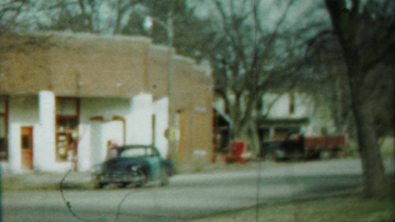 Dark sedan parked in front of a low building with white pillars and bare trees.