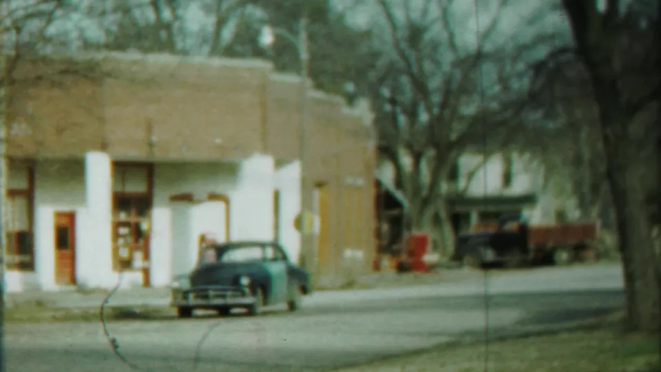 Cheyenne County, Kansas street view with a parked dark sedan, low building facade, and background pickup truck.
