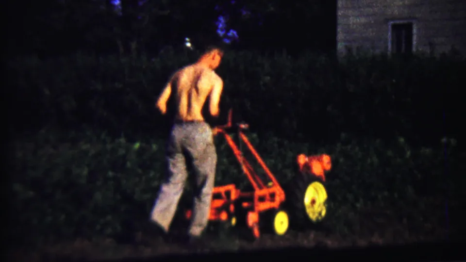 In 1958 Saint Francis, Kansas footage, a shirtless man operates a red and yellow walk-behind tiller in a dim backyard near a house.