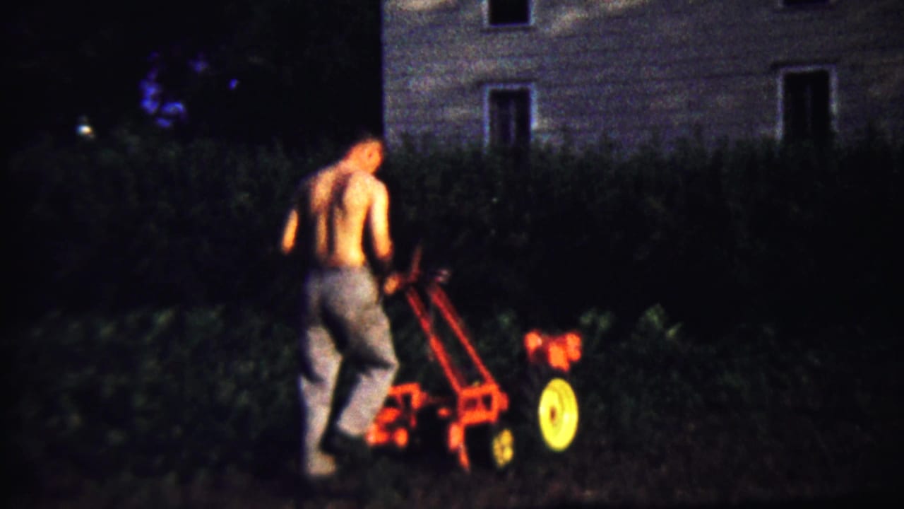 A soft 8mm frame shows the man working the red tiller near dark vegetation and a house in Saint Francis, Kansas.