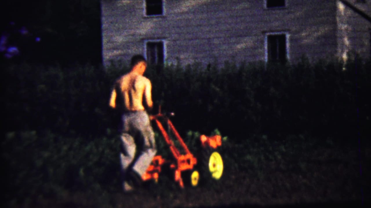 Near the end of the clip, the man guides the tiller forward in low light, framed by a hedge and residential exterior.
