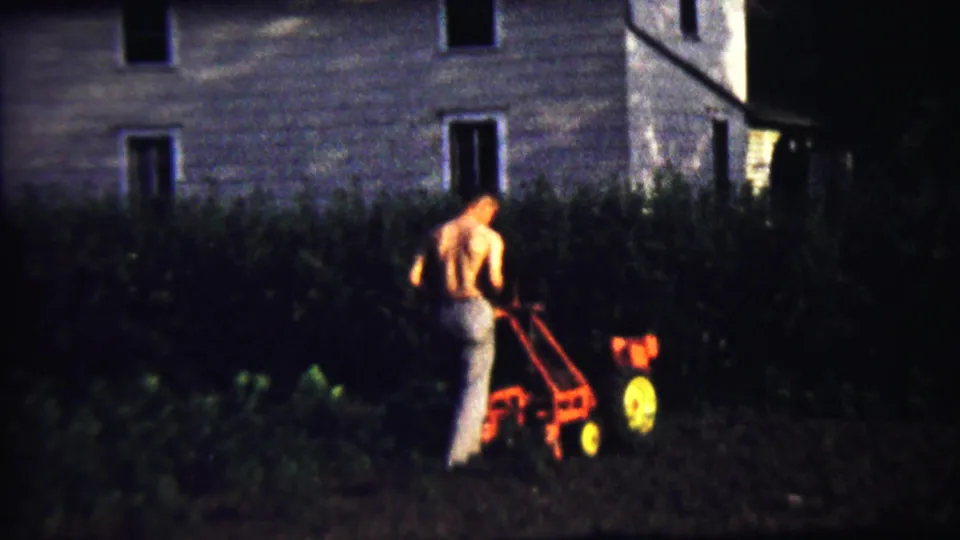 In Saint Francis, Kansas, 1958, a shirtless man guides a red tiller through a dark garden beside a light-colored house.