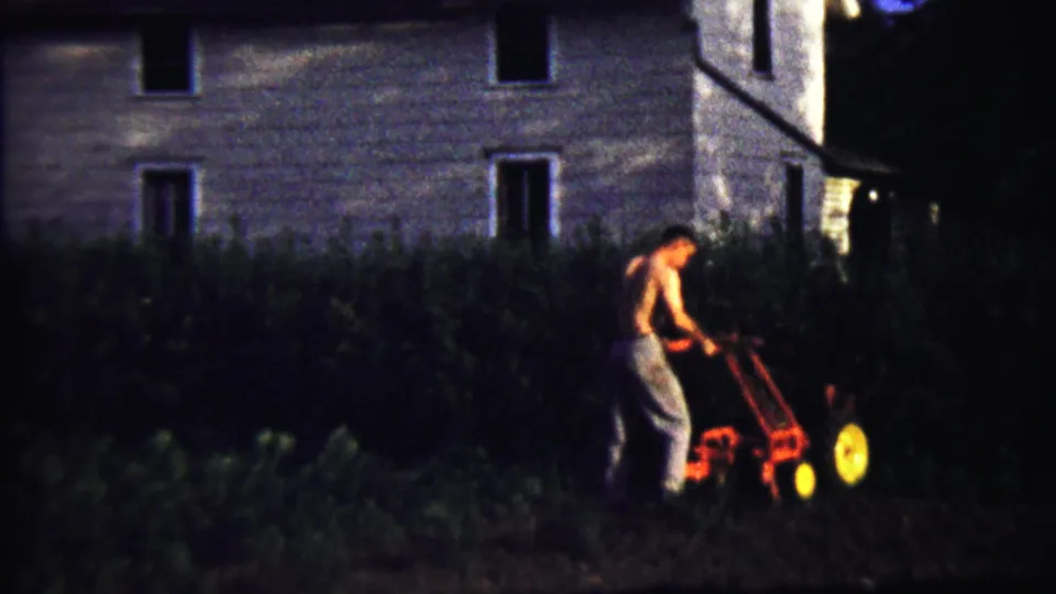 A 1958 home-movie frame shows the man standing behind the tiller, working soil near dense foliage and a modest Kansas house.