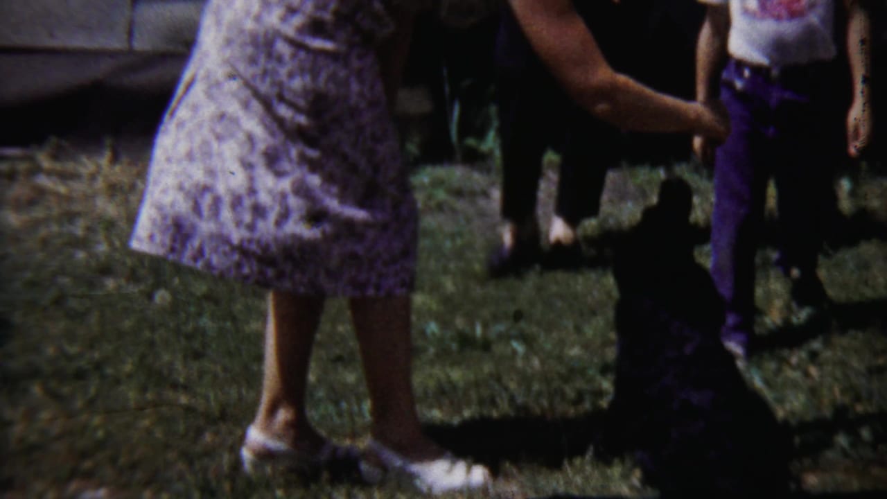 1958 Saint Francis, Kansas home-movie frame with a woman, a black dog, and partially visible family members on a grassy yard.