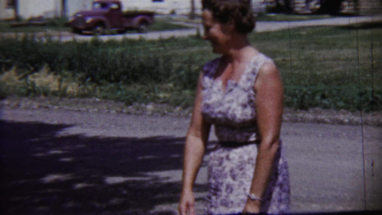 Adult woman turns in profile while walking along a quiet Saint Francis, Kansas street, with a red pickup and lawn behind her.