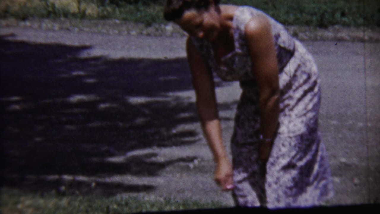 Woman in a patterned dress bends forward on a sunlit residential street.
