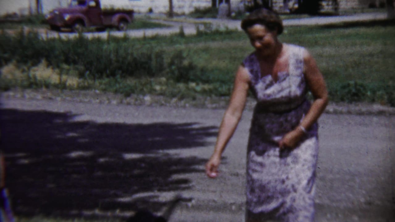 The woman appears to smile while gesturing downward on a residential street in 1958 Saint Francis, Kansas.