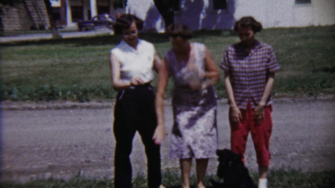 The final frame shows three women outdoors in Saint Francis, Kansas, with a black dog near their feet on a sunny residential street.